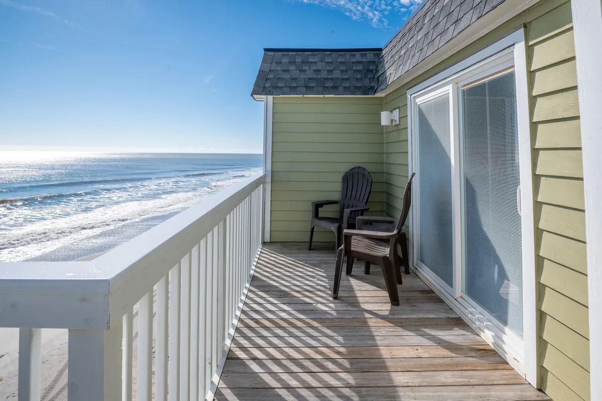 A serene private deck with wooden chairs overlooking the vast ocean. The balcony invites guests to unwind with sunrise coffee or sunset conversations, with gentle waves forming the perfect backdrop.