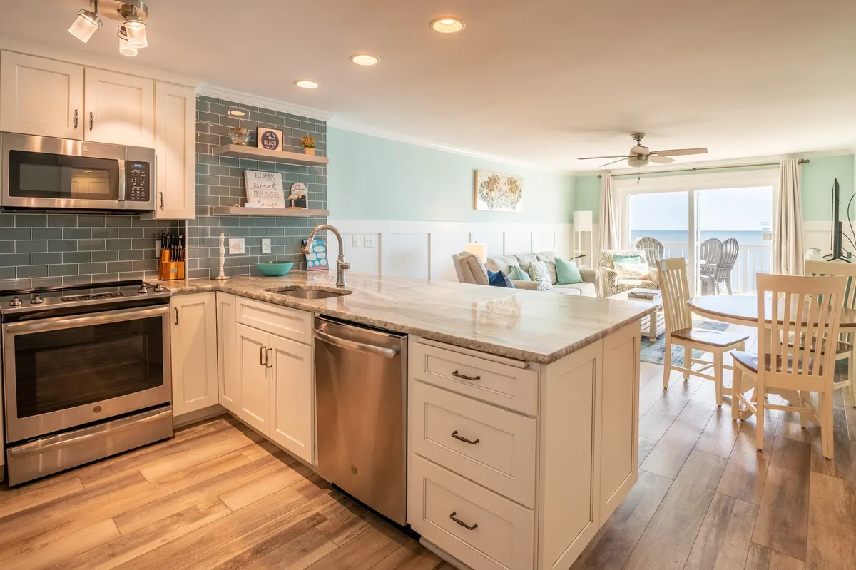 A modern, open kitchen with a spacious island and bar seating for four, stainless steel appliances, and an open sightline leading into the adjoining living area. The space is filled with natural light, creating a welcoming environment for cooking and entertaining.