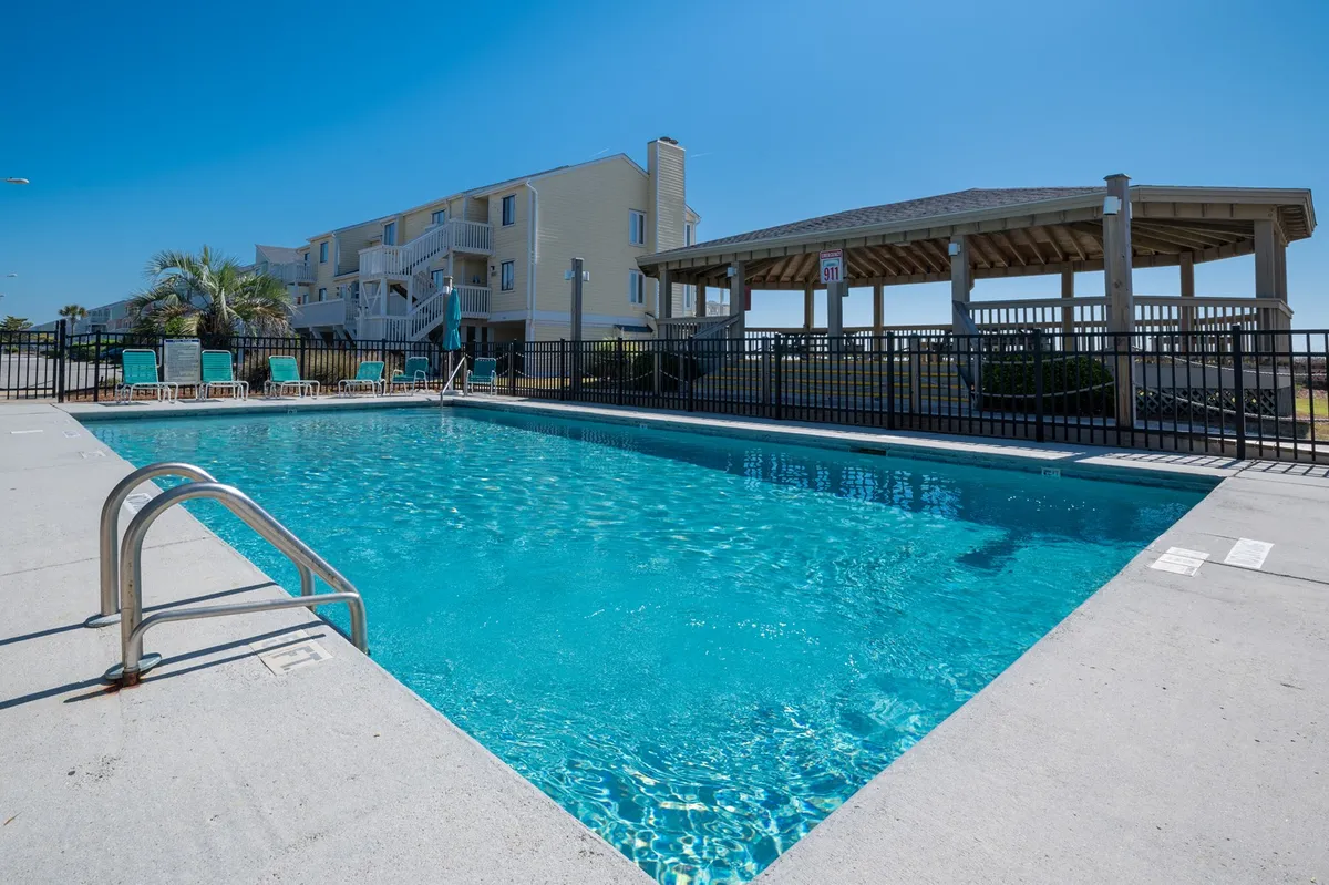 A spacious outdoor pool area featuring lounge chairs, a gazebo, and surrounding palm trees. The scene is relaxed and open, suggesting ample space for groups to gather, swim, or lounge together. The sunset ambiance adds a sense of leisure and vacation escape.