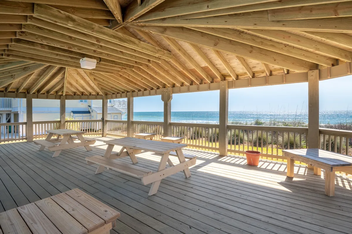 An exterior shot capturing wooden picnic tables with an open view of the ocean and direct beach access just beyond. The setup invites families to gather for picnics, watch sunsets, or head straight to the sand for more adventure.