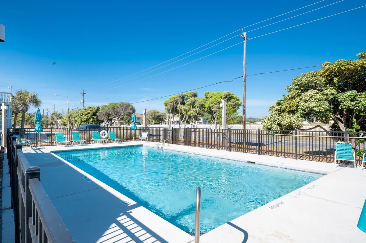 An inviting outdoor swimming pool surrounded by comfortable lounge chairs, mature trees, and secure fencing. The pool area exudes a leisurely mood, perfect for swimming, sunbathing, or gathering with friends, especially during sunset or morning yoga.