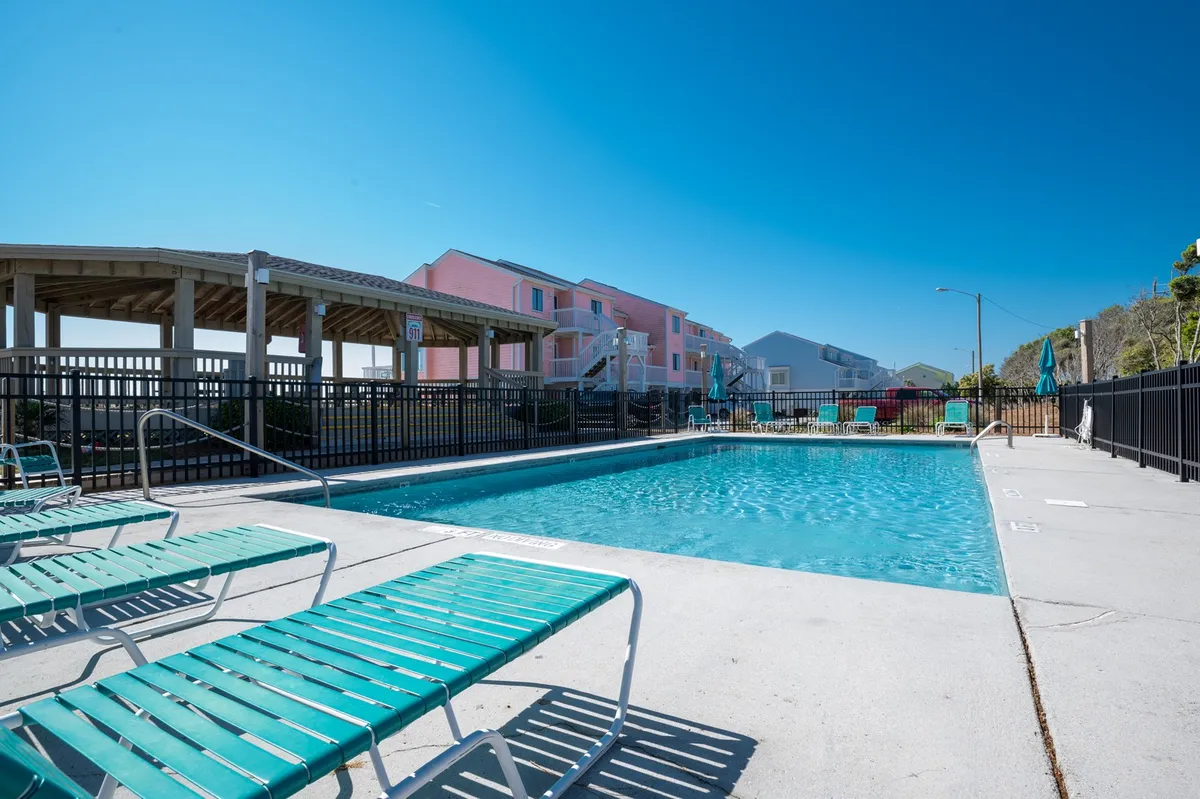 A vibrant exterior scene featuring the resort’s swimming pool surrounded by colorful building facades and an inviting array of lounge chairs. The area is lively yet relaxing, with space for sunbathing, swimming, and gathering as a family.