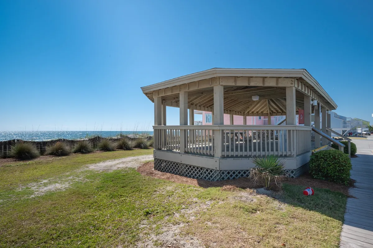 A serene oceanfront gazebo set on landscaped grass with open views of the sea. The space is ideal for gathering with friends, enjoying the coastal breeze, or relaxing in a tranquil setting. The mood is peaceful, perfect for sunset picnics or stargazing.