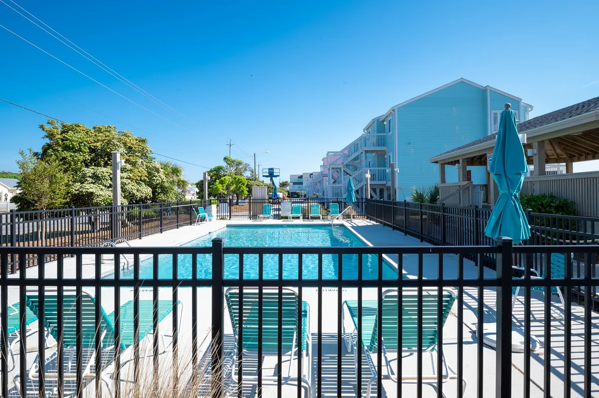 A sparkling swimming pool surrounded by lounge chairs and large umbrellas, set against a backdrop of lush, manicured greenery. The open sky above and surrounding plants give the impression of a tranquil outdoor retreat—perfect for relaxing after wildlife excursions or sunrise strolls.