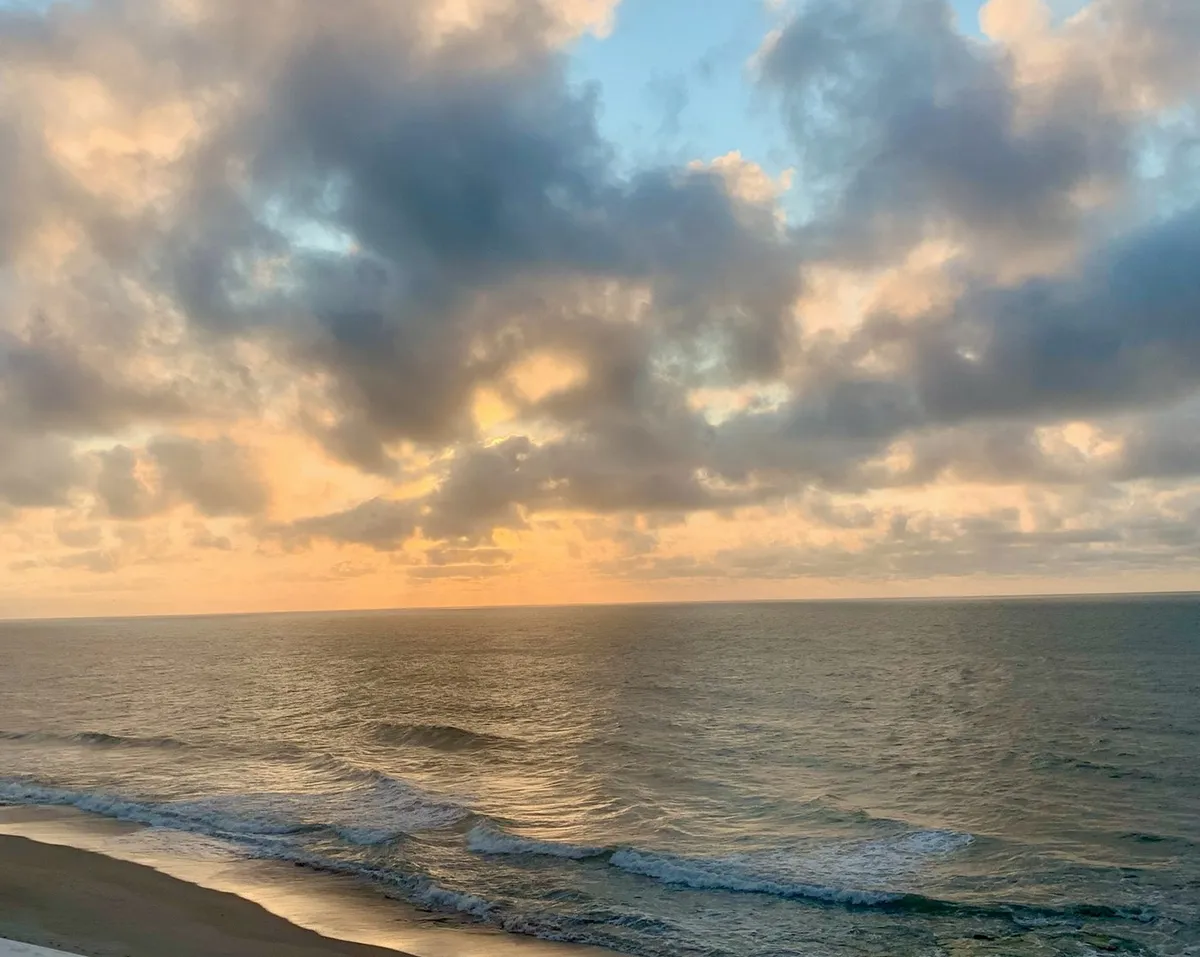 A stunning view of the ocean at sunset, with waves rolling in under a dramatic sky filled with colorful cloud formations. The scene invites guests to imagine tranquil beachfront walks and the soothing sound of the sea.